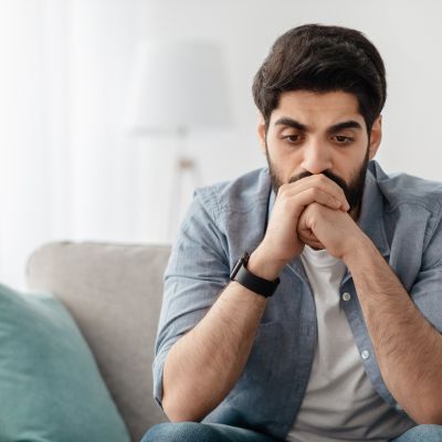 Ein sitzender Mann stützt den Kopf auf die Hände.
